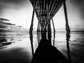 Low section of pier silhouette by sea against sky