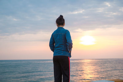 Rear view of man standing against sea during sunset