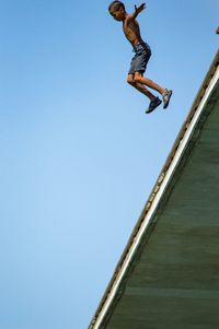 Low angle view of man jumping against clear blue sky