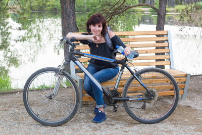 A brunette woman of 35-40 years old, riding a bicycle, sat down to rest on a bench in a park by 