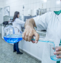 Midsection of scientist pouring liquid in beaker at laboratory