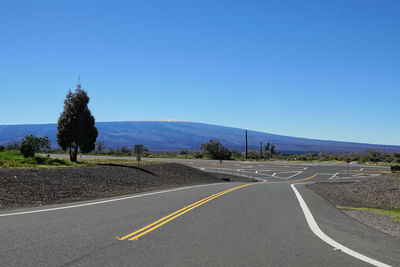 Road amidst field against clear blue sky