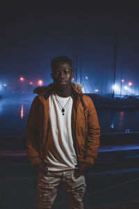 Portrait of young man standing at harbor in night