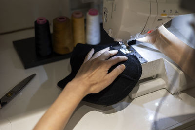 Woman is sewing black beanie hat on a sewing machine, using a sewing machine on the sewing table