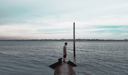 Side view of man standing on rock in lake against sky