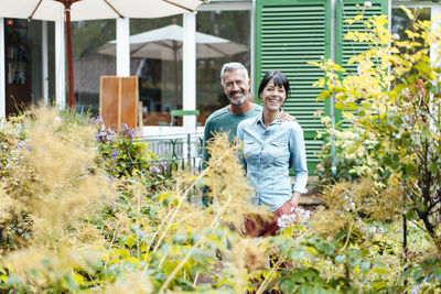 Happy man arm around woman amidst plants in backyard