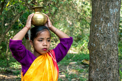 A tribal teenage girl is walking in the woods to fetch water in a brass pitcher