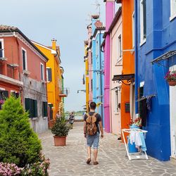 Rear view of traveler walking on alley amidst multi colored buildings at burano