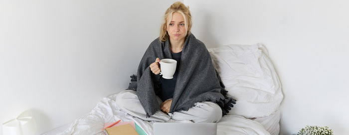 Portrait of young woman sitting on bed at home