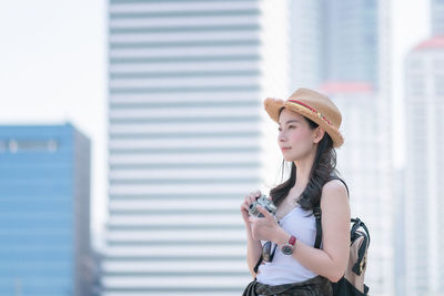 Portrait of young woman wearing hat standing against built structure
