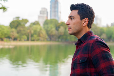 Young man looking away while standing by lake