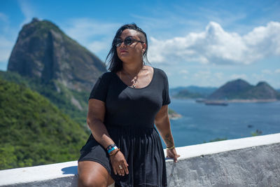 Young woman wearing sunglasses standing on mountain against sky