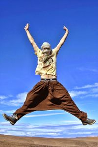 Low angle view of man jumping against blue sky