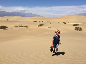 Boy walking on sand dune in desert against sky