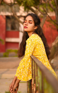 Young woman with eyes closed standing by railing on footpath