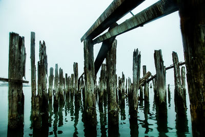 Close-up of wooden posts in lake against sky