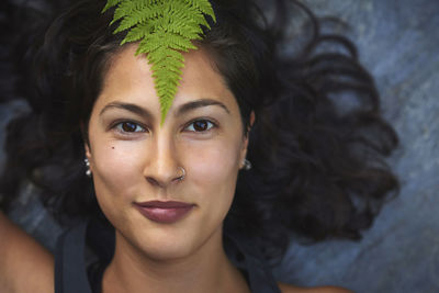 Woman with a fern on her face. she's lying on a rock and covers half her face with a fern leaf.