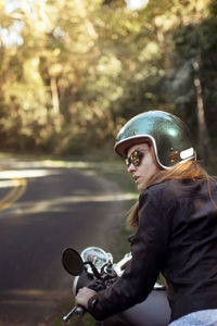 Young woman in jacket riding motorcycle on road