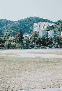 Trees on field by buildings against sky