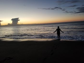 Silhouette man standing on beach against sky during sunset