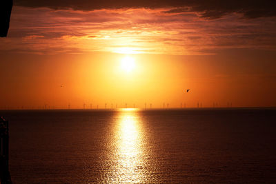 Scenic view of sea against orange sky wind turbines off shore llandudno 