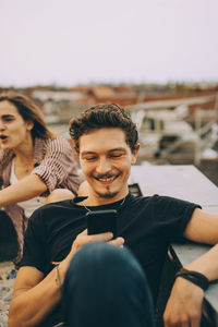 Young man using smart phone while friend enjoying at rooftop party