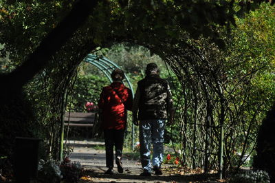 Rear view of woman and man walking on covered footpath amidst plants at park