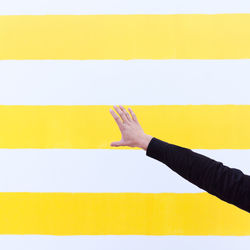 Cropped hand by yellow and white wall