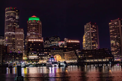 Illuminated buildings by river against sky at night