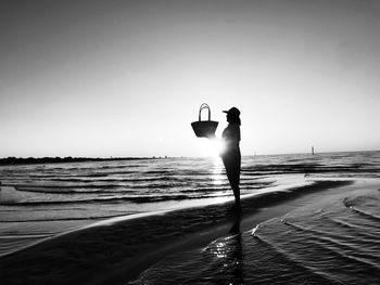 Silhouette woman with bag standing on beach against sky