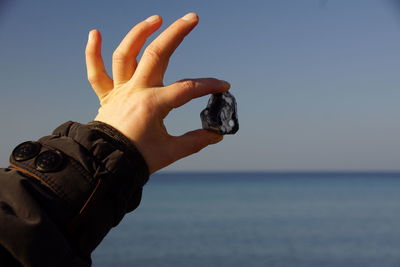 Close-up of hand holding stone against clear sky