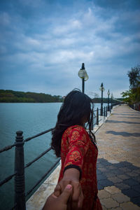 Cropped image of boyfriend holding girlfriend hands on footpath by lake