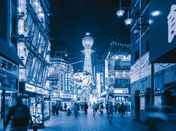 People walking on illuminated street amidst buildings in city at night