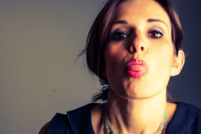 Close-up portrait of beautiful woman sticking out tongue against gray background