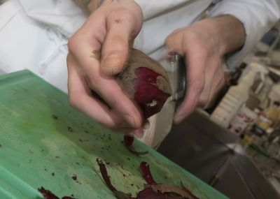 Cook is peeling beetroots with a peeler in the kitchen