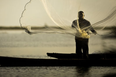 Fisherman casting fishing net in lake during sunset