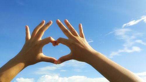 Low angle view of hands holding heart shape against sky