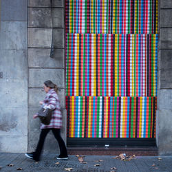 Side view of woman walking against colorful closed shutter