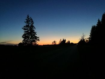 Silhouette trees on field against clear sky at sunset