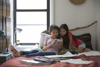 Happy sisters looking at smart phone on bed at home