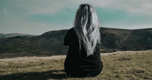 Rear view of woman sitting on field against sky