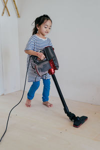 Cute little girl cleaning wooden floor with vacuum cleaner