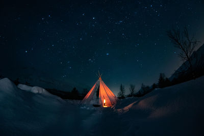 Tent on snow covered field against sky at night