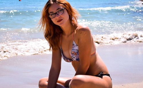 Portrait of smiling woman in bikini sitting on shore at beach