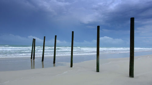 Wooden posts on beach against sky