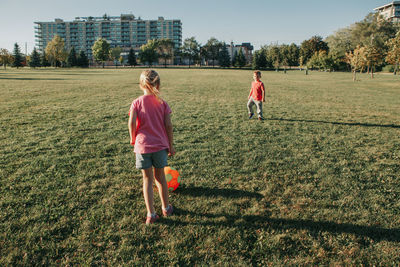 Girl and boy friends playing soccer football on playground grass field outside. 