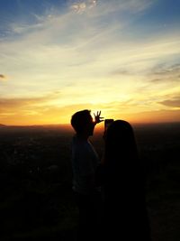 Man and woman with phone standing against sky during sunset