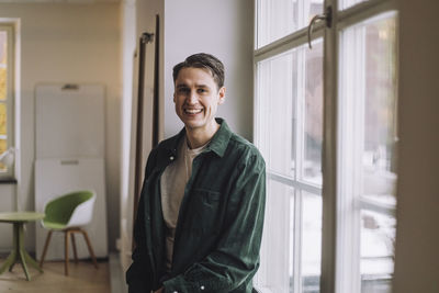 Portrait of happy male phd student leaning by window in innovation lab