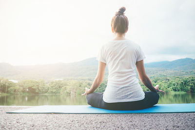 Woman doing yoga at lakeshore against sky