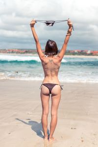Rear view of seductive woman standing at beach against sky